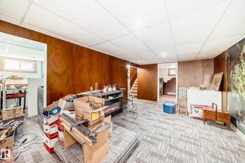 Finished basement space featuring panel walls, patterned carpet flooring, a drop ceiling with recessed lighting, and an electric fireplace with a mantel - 11303 60 Street, Edmonton, AB - Indoor