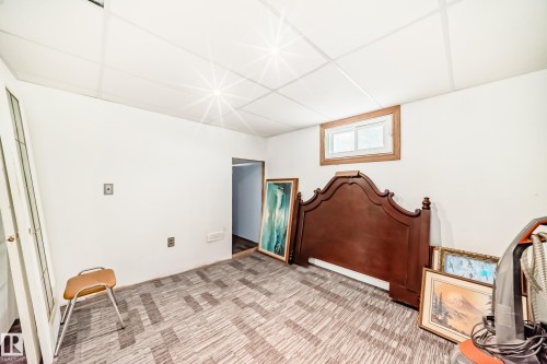 Lower-level room featuring patterned carpet flooring, a drop ceiling, white painted walls, and a wood-trimmed window - 11303 60 Street, Edmonton, AB - Indoor Photo Showing Other Room