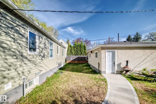Manicured side yard featuring a concrete pathway, a stucco-finished accessory dwelling unit with a single white entry door, and a horizontal siding main residence with white trim windows - 11303 60 Street, Edmonton, AB - Outdoor
