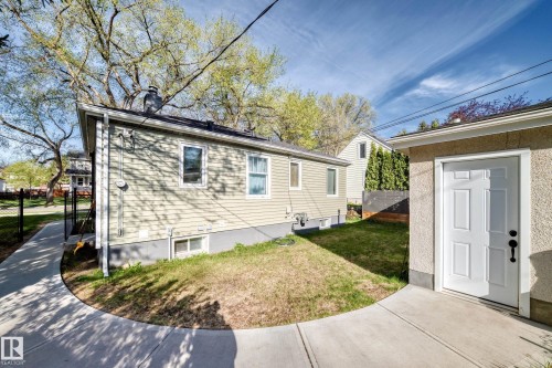 Exterior siding with multiple windows, concrete walkway, and a detached stucco structure with a white door - 11303 60 Street, Edmonton, AB - Outdoor