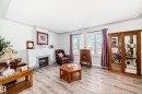 Living space featuring wood-finish flooring, a white mantel fireplace with a stone-look surround, and multiple windows with curtain rods - 11303 60 Street, Edmonton, AB  - Indoor Photo Showing Living Room With Fireplace 
