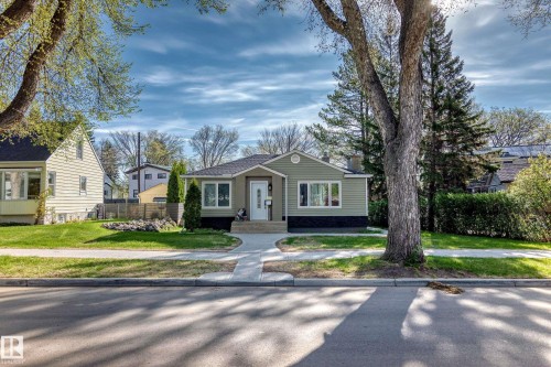 Siding exterior home with a partial stone facade, a concrete sidewalk leading to the front entry, and a manicured lawn - 11303 60 Street, Edmonton, AB - Outdoor With Facade
