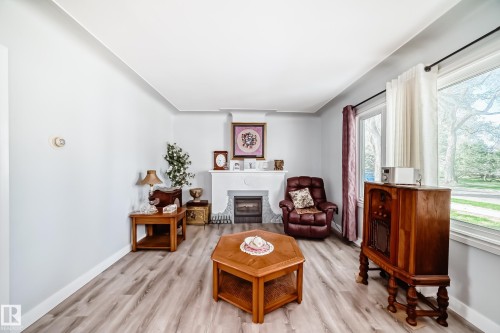 Living area featuring a white mantel fireplace with a black grate, light wood-finish flooring, and white baseboards - 11303 60 Street, Edmonton, AB - Indoor Photo Showing Living Room With Fireplace