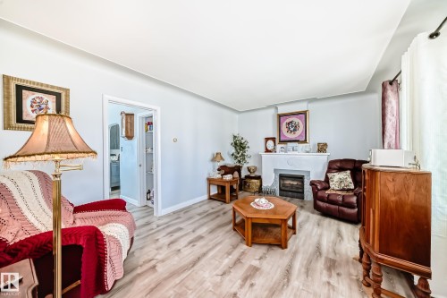 Living area featuring wood-finish flooring and a white decorative fireplace with an electric insert - 11303 60 Street, Edmonton, AB - Indoor Photo Showing Other Room With Fireplace