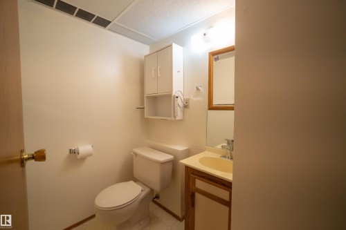 Compact bathroom featuring a neutral color palette, built-in vanity with a single sink, wood-framed mirror, and overhead cabinet storage - 4724 38B Avenue Nw, Edmonton, AB - Indoor Photo Showing Bathroom
