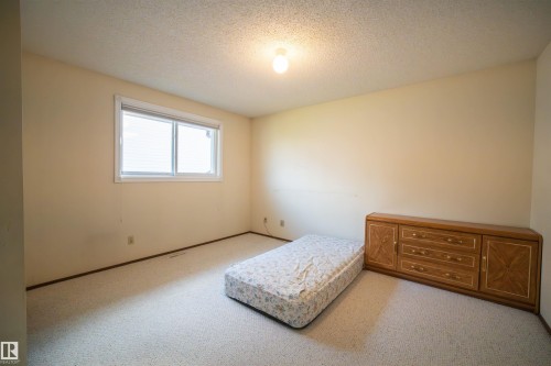 Carpeted room with a double-pane window featuring white blinds, neutral painted walls, and a textured ceiling - 4724 38B Avenue Nw, Edmonton, AB - Indoor