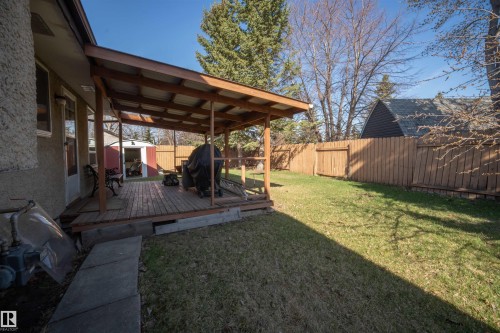 Expansive backyard featuring a covered wood deck, wood privacy fence, and a red and white shed - 4724 38B Avenue Nw, Edmonton, AB - Outdoor