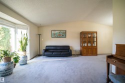 Spacious living area featuring a large bay window, vaulted ceilings, and light-toned carpeting - 