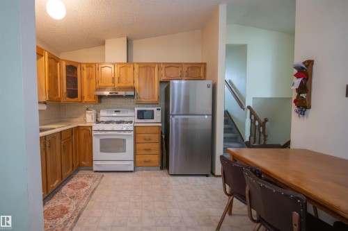 Kitchen with wood-finish cabinetry, white appliances, and a stainless steel refrigerator - 4724 38B Avenue Nw, Edmonton, AB - Indoor Photo Showing Kitchen
