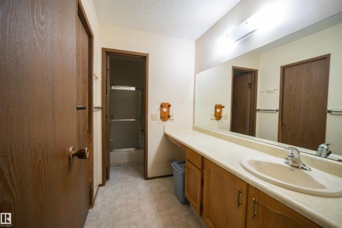 Bathroom featuring a long vanity with a single sink, light-toned countertop, and wood-finish cabinetry - 4724 38B Avenue Nw, Edmonton, AB - Indoor Photo Showing Bathroom