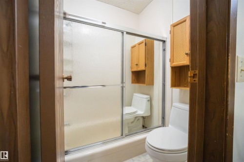 White toilet and built-in wood cabinetry with a textured door panel - 4724 38B Avenue Nw, Edmonton, AB - Indoor Photo Showing Bathroom