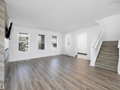 This bright living area features light wood-look flooring, white walls, and multiple windows providing natural light - 9852 217 Street, Edmonton, AB - Indoor Photo Showing Living Room