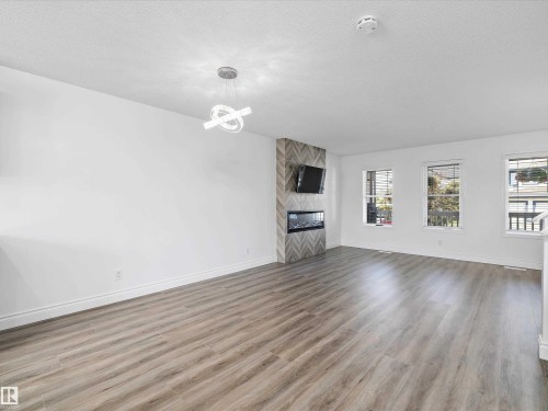 Spacious living area featuring light-colored flooring, a modern fireplace with a tiled surround, and multiple windows providing natural light - 9852 217 Street, Edmonton, AB - Indoor Photo Showing Living Room With Fireplace