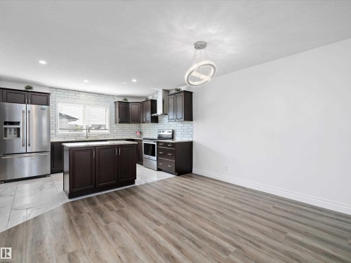 Kitchen featuring dark wood cabinetry, a central island with a granite countertop, a subway tile backsplash, and stainless steel appliances - 9852 217 Street, Edmonton, AB - Indoor Photo Showing Kitchen With Upgraded Kitchen