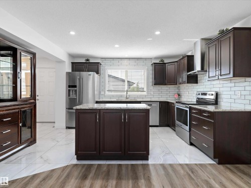 The kitchen features dark wood cabinetry, stainless steel appliances, granite countertops, and a white subway tile backsplash - 9852 217 Street, Edmonton, AB - Indoor Photo Showing Kitchen With Upgraded Kitchen