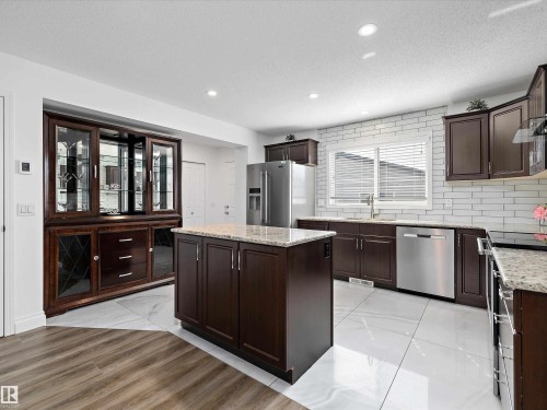 The kitchen features dark wood cabinetry, stainless steel appliances, granite countertops, and white subway tile backsplash - 9852 217 Street, Edmonton, AB - Indoor Photo Showing Kitchen With Upgraded Kitchen