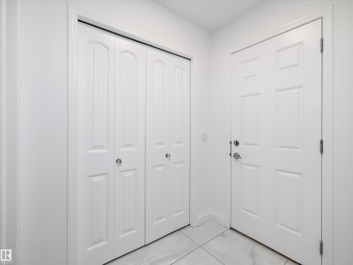 Entryway featuring a white paneled door and bifold closet doors, complemented by white tile flooring - 9852 217 Street, Edmonton, AB - Indoor Photo Showing Other Room