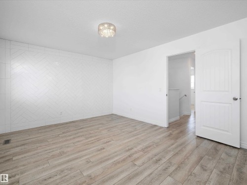 This bright room features light-toned wood-style flooring, a decorative tiled accent wall in a herringbone pattern, and a stylish ceiling light fixture - 9852 217 Street, Edmonton, AB - Indoor Photo Showing Other Room