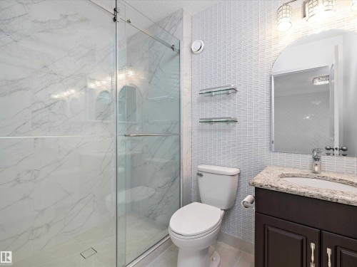 This bathroom features a shower with sliding glass doors and white marble-style tiling, a toilet, and a vanity with a granite countertop and a framed mirror - 9852 217 Street, Edmonton, AB - Indoor Photo Showing Bathroom