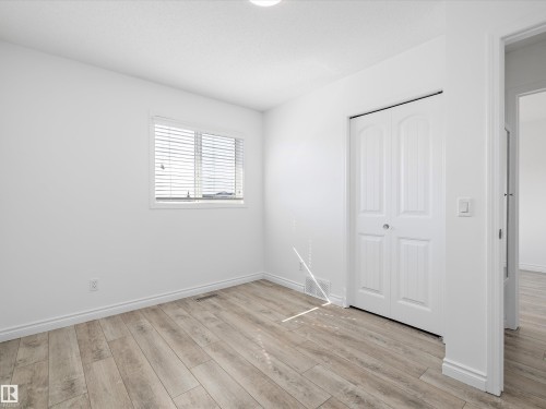 This bright room features a window with blinds, light-toned wood-look flooring, and a closet with bifold doors - 9852 217 Street, Edmonton, AB - Indoor Photo Showing Other Room