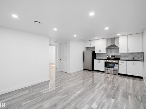 The property features a kitchen with white cabinetry, stainless steel appliances, and a tiled backsplash, alongside light-colored flooring - 9852 217 Street, Edmonton, AB - Indoor Photo Showing Kitchen
