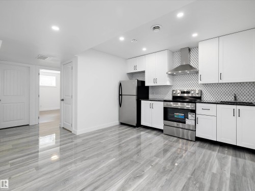 The kitchen features white cabinetry, stainless steel appliances, a tile backsplash, and dark countertops - 9852 217 Street, Edmonton, AB - Indoor Photo Showing Kitchen