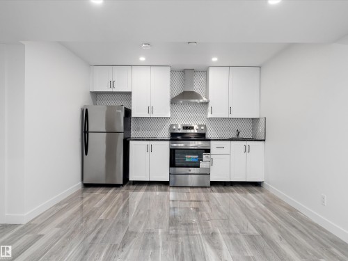 The kitchen features stainless steel appliances, white cabinetry, and a patterned tile backsplash - 9852 217 Street, Edmonton, AB - Indoor Photo Showing Kitchen