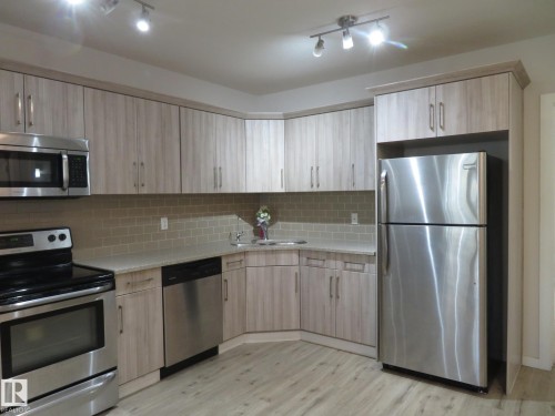 Kitchen featuring wood-finish cabinetry, stainless steel appliances, light-toned countertops, and a subway tile backsplash - 11840B 122 Street, Edmonton, AB - Indoor Photo Showing Kitchen With Stainless Steel Kitchen