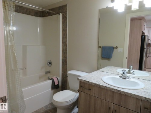 Bathroom featuring a built-in tub with tile surround, a single vanity with an oval basin, a chrome faucet, and a wall-mounted mirror - 11840B 122 Street, Edmonton, AB - Indoor Photo Showing Bathroom
