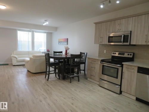 Open-concept living space featuring wood-finish flooring, recessed lighting, and large windows with vertical blinds - 11840B 122 Street, Edmonton, AB - Indoor Photo Showing Kitchen With Stainless Steel Kitchen