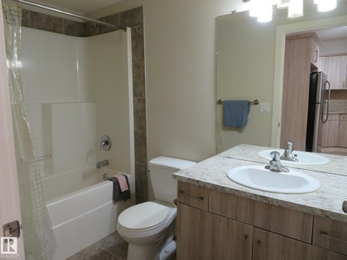 Bathroom featuring a wood-finish vanity with a single sink, an integrated tub and shower with tile surround, and tile flooring - 11840B 122 Street, Edmonton, AB - Indoor Photo Showing Bathroom