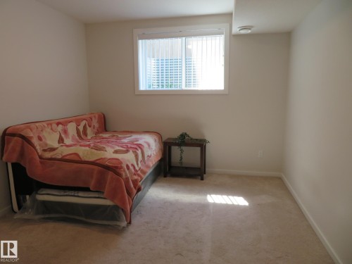 Carpeted room featuring a window with vertical blinds, light-toned walls, and a ceiling-mounted smoke detector - 11840B 122 Street, Edmonton, AB - Indoor Photo Showing Bedroom