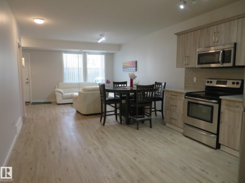 Open-concept living space featuring wood-finish flooring throughout, a kitchen with light wood-finish cabinetry, stainless steel appliances, and a tiled backsplash - 11840B 122 Street, Edmonton, AB - Indoor Photo Showing Kitchen With Stainless Steel Kitchen
