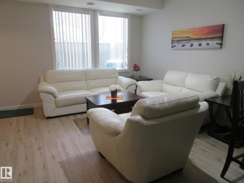 Living area featuring light wood-finish flooring and multiple windows with vertical blinds - 11840B 122 Street, Edmonton, AB - Indoor Photo Showing Living Room