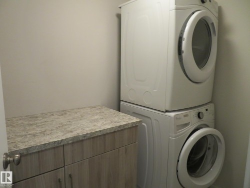 Dedicated laundry area featuring a stackable washer and dryer, light-toned wood-finish cabinetry, and a speckled countertop - 11840B 122 Street, Edmonton, AB - Indoor Photo Showing Laundry Room
