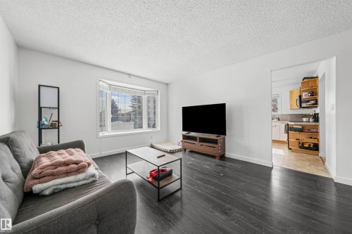 Living area featuring dark wood-finish flooring, white walls, and a bay window - 115 Warwick Road, Edmonton, AB - Indoor Photo Showing Living Room