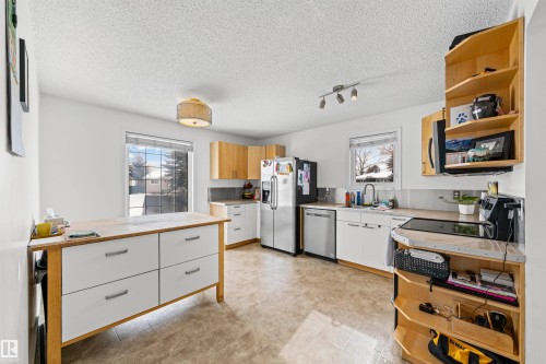Kitchen featuring stainless steel appliances, wood-finish cabinetry, a central island with white drawers, and tile flooring - 115 Warwick Road, Edmonton, AB - Indoor Photo Showing Kitchen