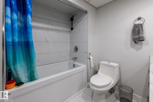 Full bathroom featuring a white bathtub with a tiled surround, a chrome shower system, a white toilet, and light-toned walls - 3004 68 Street, Edmonton, AB - Indoor Photo Showing Bathroom