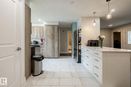 Kitchen featuring a large central island with a light-toned countertop, white cabinetry with silver hardware, white tile flooring, and wood-finish cabinetry - 3004 68 Street, Edmonton, AB - Indoor