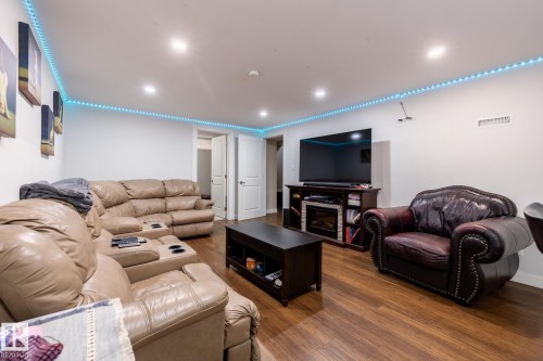 Spacious recreation room featuring wood-finish flooring, recessed lighting, and an entertainment console with a built-in electric fireplace - 3004 68 Street, Edmonton, AB - Indoor Photo Showing Living Room With Fireplace