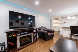 Open-concept living space featuring wood-finish flooring, recessed lighting, and a built-in media console with a stone-accented electric fireplace - 