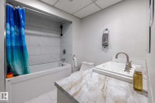 Bathroom featuring a bathtub with subway tile surround, white vanity with an undermount sink, brushed nickel faucet, and light-toned countertop - 3004 68 Street, Edmonton, AB - Indoor Photo Showing Bathroom