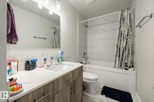 Bathroom featuring a wood-finish vanity with a single basin, a white countertop, and a built-in bathtub with subway tile surround - 3004 68 Street, Edmonton, AB - Indoor Photo Showing Bathroom