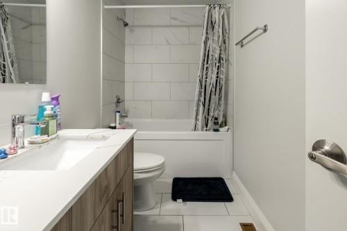 Bathroom featuring a white bathtub, white subway-style tile surround, a single vanity with wood-finish cabinetry, white countertop, and a chrome faucet - 3004 68 Street, Edmonton, AB - Indoor Photo Showing Bathroom
