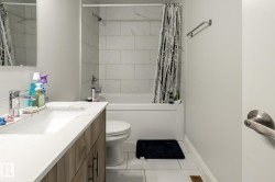 Bathroom featuring a white bathtub, white subway-style tile surround, a single vanity with wood-finish cabinetry, white countertop, and a chrome faucet - 
