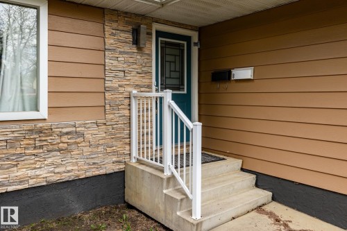 Entryway featuring a teal door with decorative glass, stone veneer accents, concrete steps, and white railings - 3004 68 Street, Edmonton, AB - Outdoor With Exterior