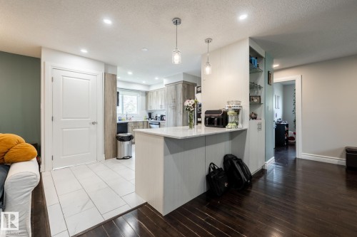 Contemporary kitchen featuring a white countertop island with pendant lighting, recessed ceiling lights, wood-finish cabinetry, and a window above the sink - 3004 68 Street, Edmonton, AB - Indoor Photo Showing Kitchen