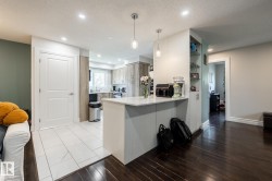 Contemporary kitchen featuring a white countertop island with pendant lighting, recessed ceiling lights, wood-finish cabinetry, and a window above the sink - 