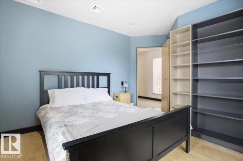 Light wood-finish flooring with blue painted walls and dark baseboards - 8709 92A Avenue, Edmonton, AB - Indoor Photo Showing Bedroom