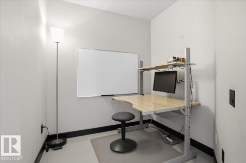 Dedicated workspace featuring a wall-mounted whiteboard, a built-in corner desk with a light wood-finish surface, and a wall-mounted monitor arm - 8709 92A Avenue, Edmonton, AB - Indoor